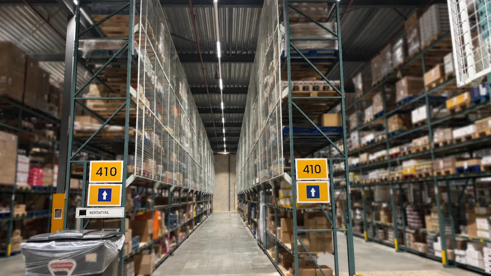 Hoge palletstellingen met een witte gaasachterwand als doorvalbeveiliging langs een magazijngang