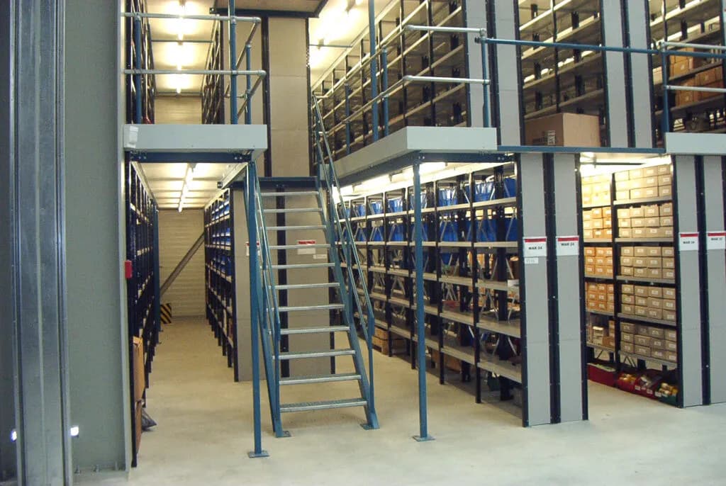 Bordesvloer met leuningwerk en trap boven legbordstellingen in een magazijn